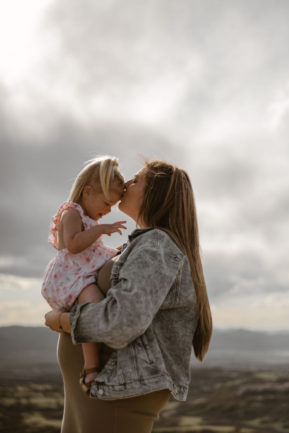 A tender moment between parent and child against a cloudy mountain landscape.