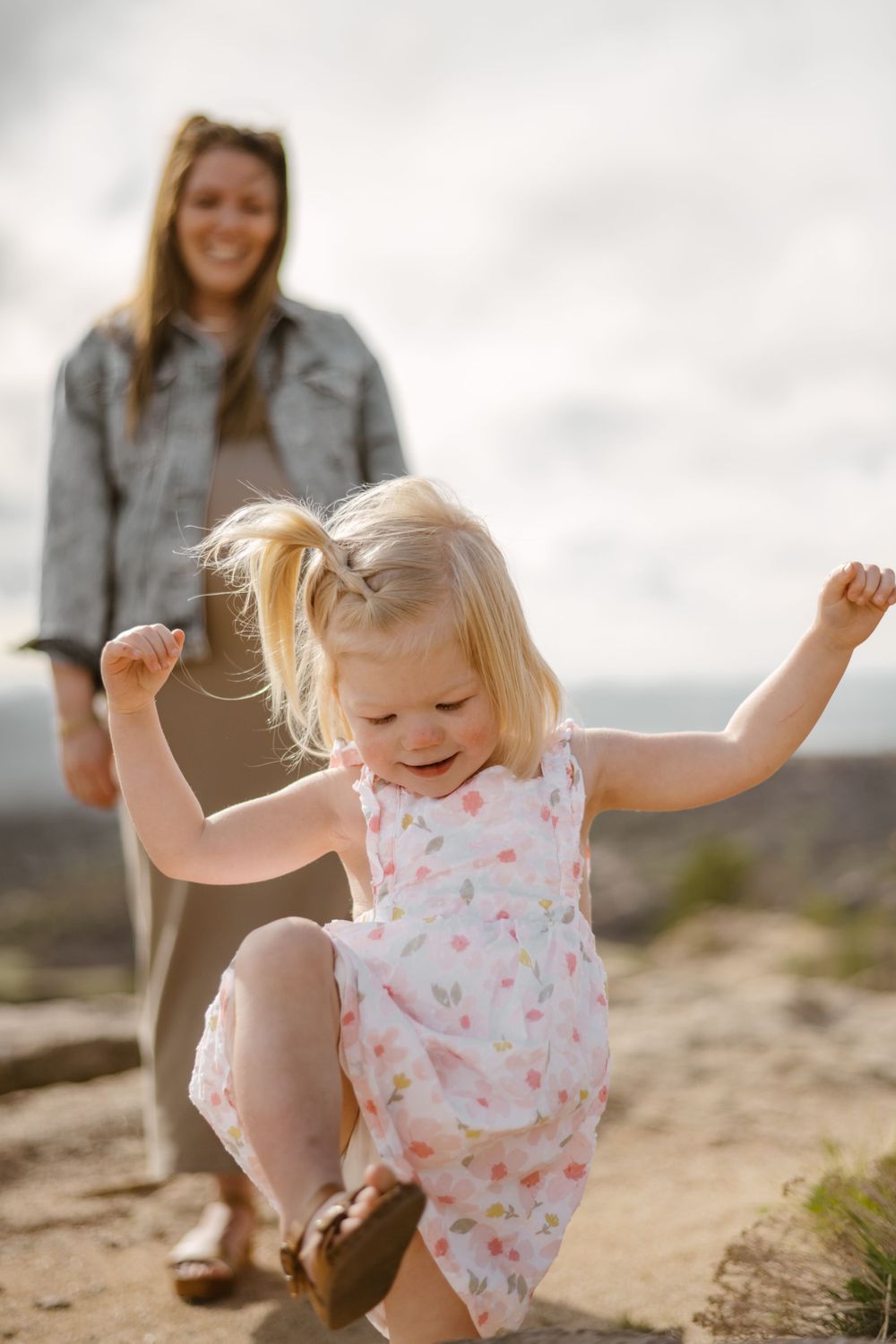 Young child in floral dress dances joyfully outdoors with arms raised.