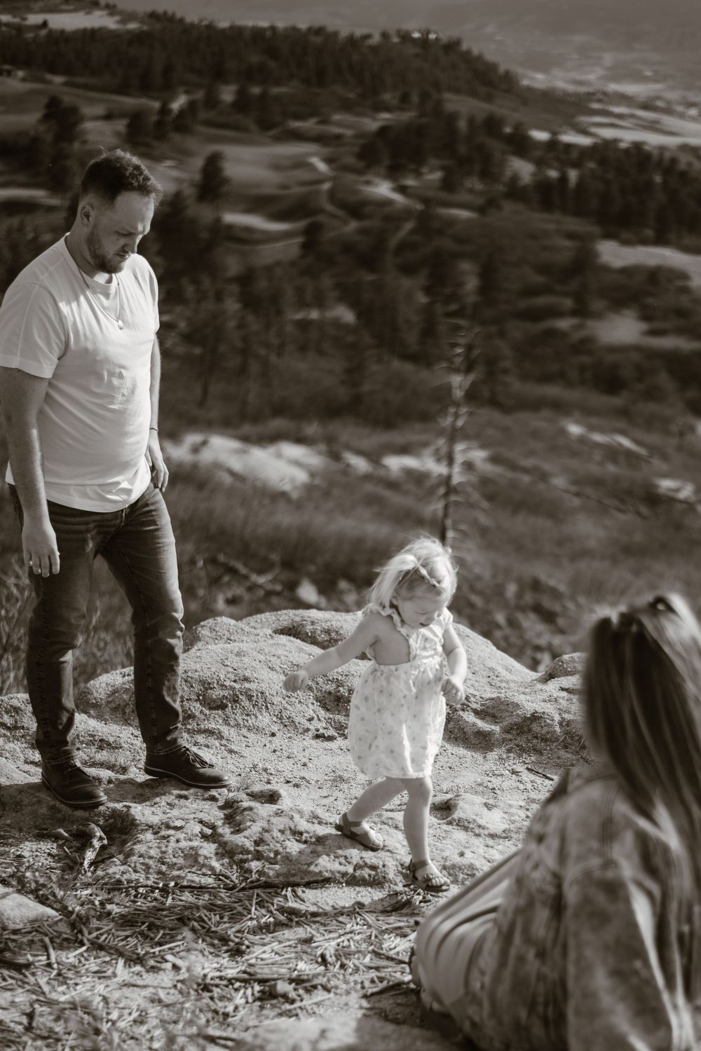 Family enjoying time together on rocky hillside in black and white.