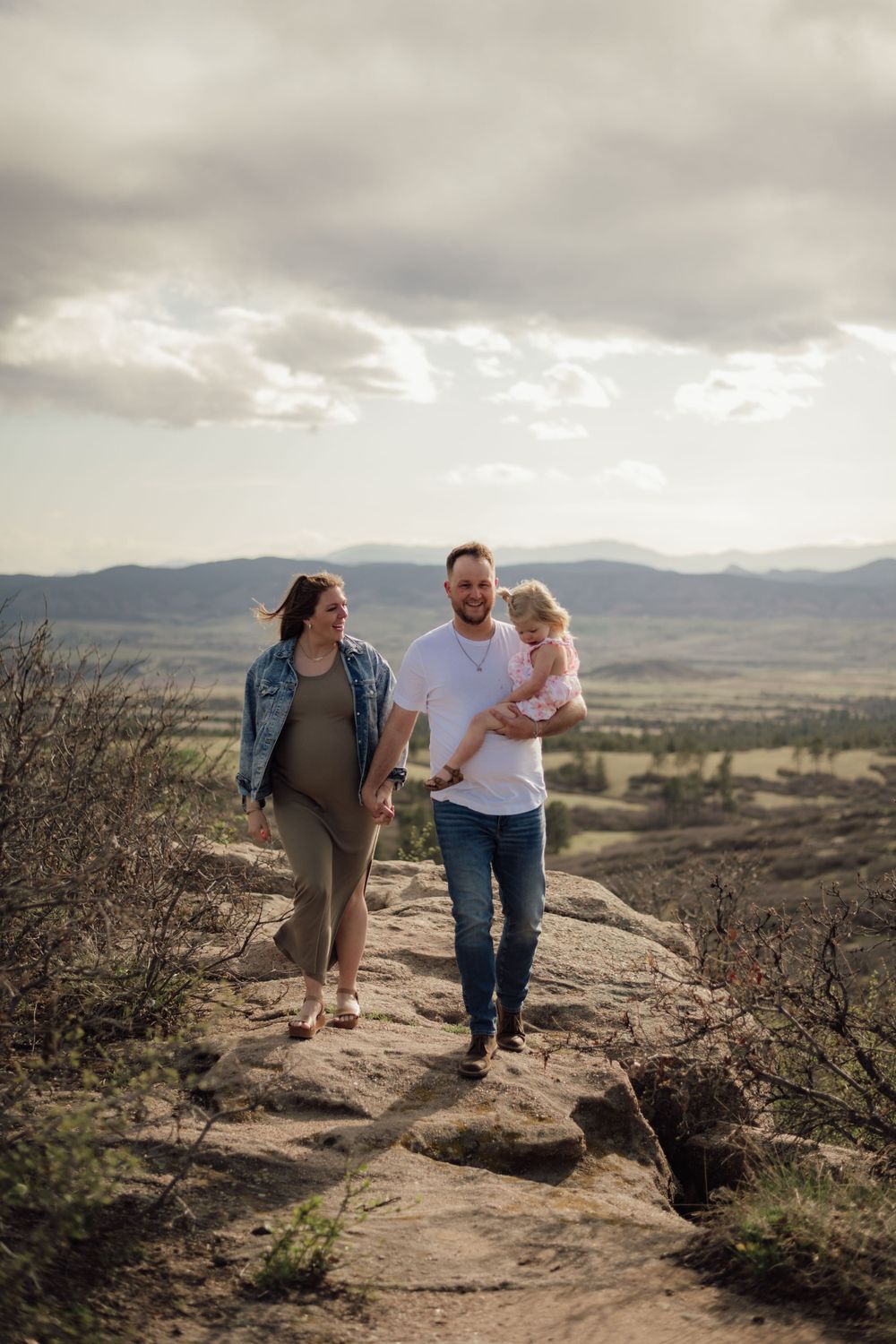Family hiking together on rocky mountain trail under cloudy skies.