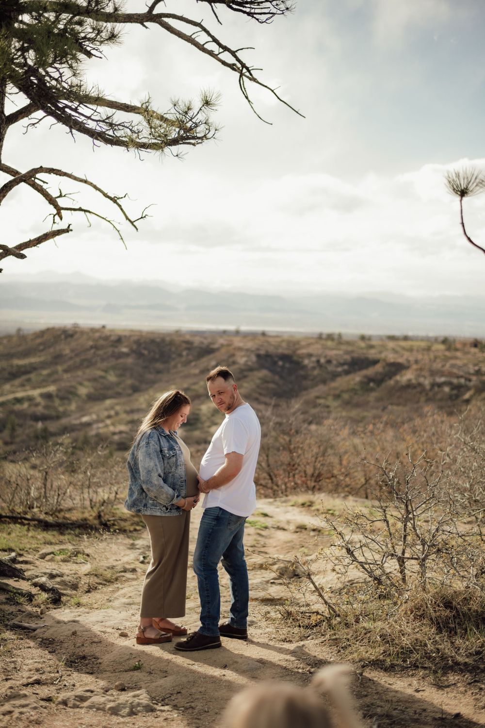 A romantic photoshoot on a rugged hilltop with dramatic cloudy skies in the background.