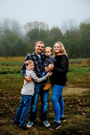 A family poses together outdoors on a misty autumn day in a field with trees in the background.