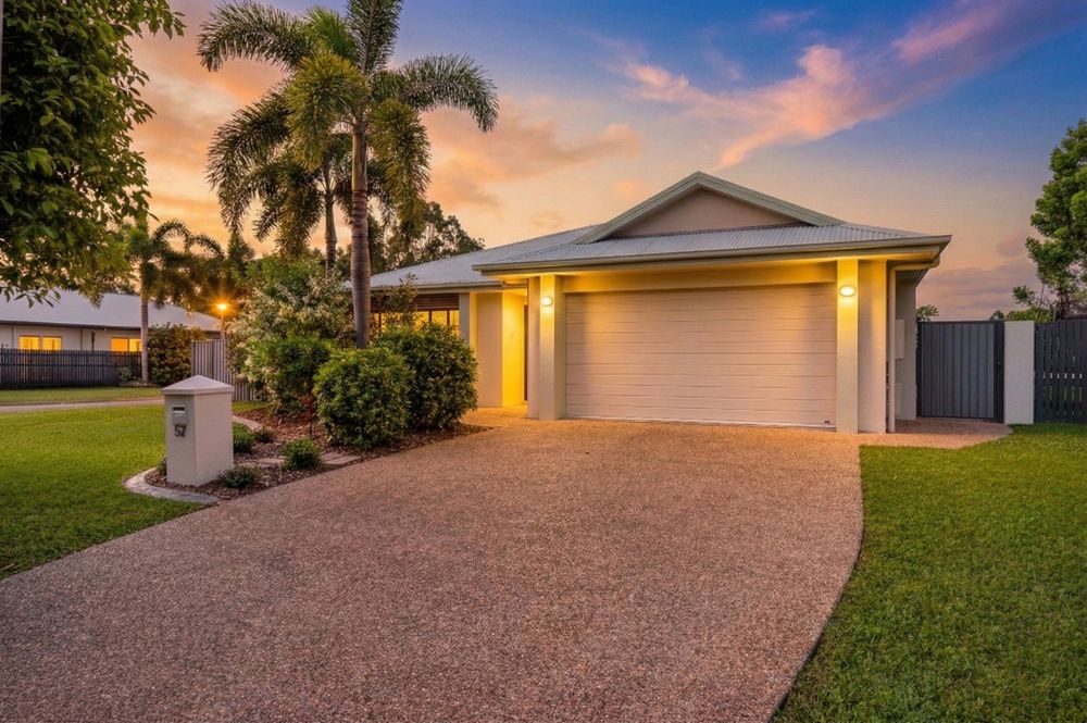 Contemporary suburban home with palm trees and exposed aggregate driveway at sunset.