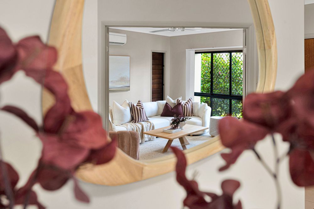 Modern white bedroom interior with burgundy orchid flowers in foreground and large windows letting in natural light.