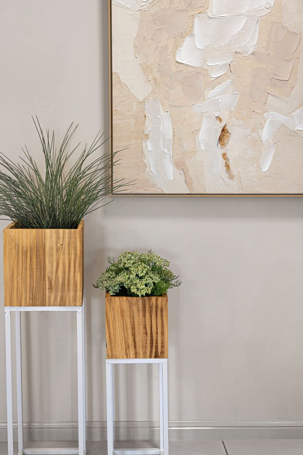 Abstract beige artwork with white textural elements above wooden plant stands with greenery.