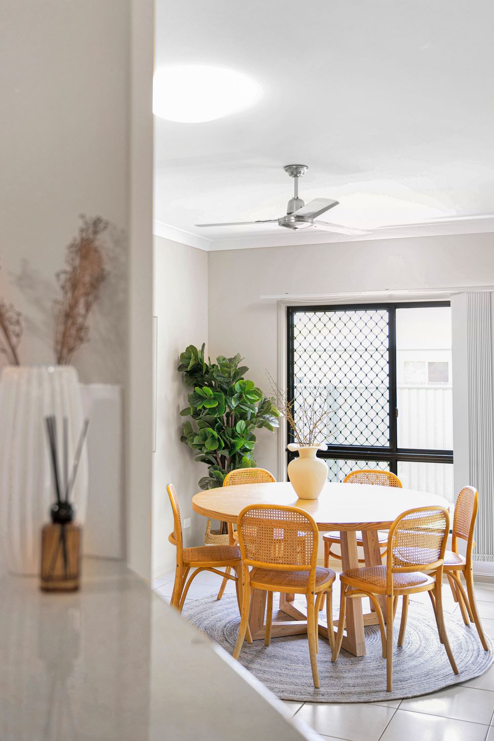 Bright dining area with wooden table and chairs on round rug near window with natural light.