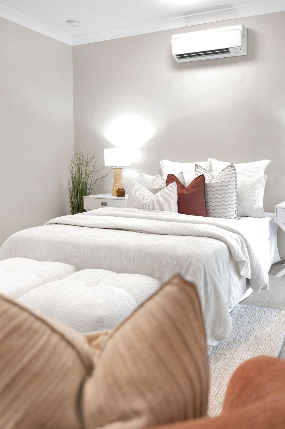 Modern bedroom interior with white bedding, beige accents, and natural lighting.
