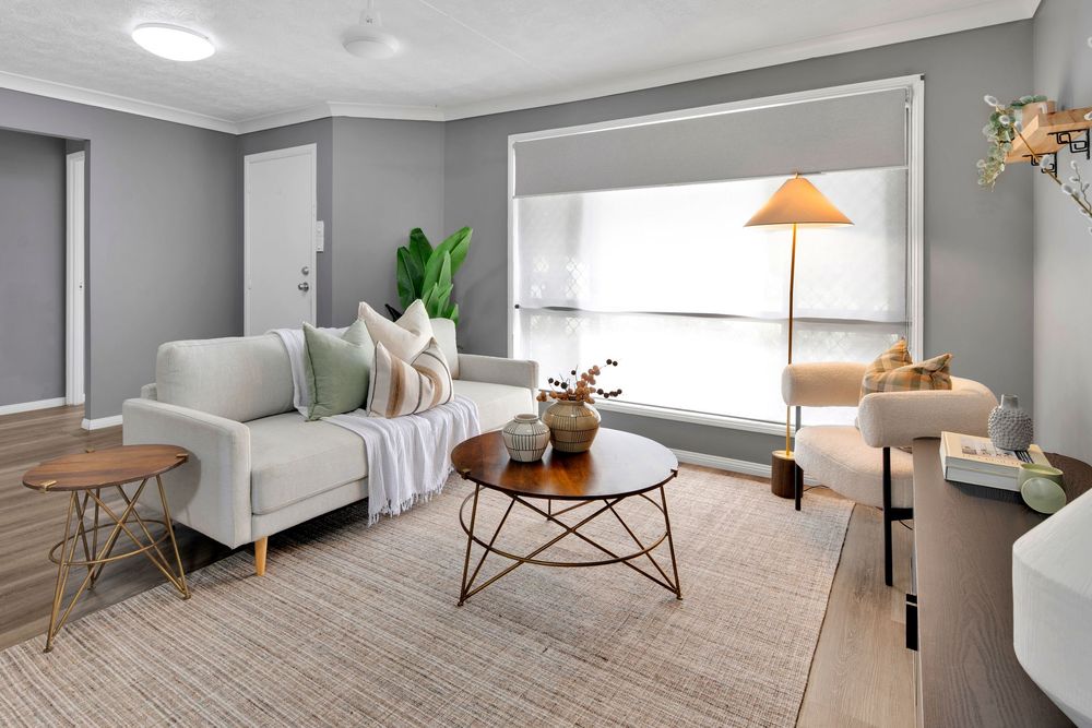 Modern minimalist living room with gray walls, white furniture, and natural light streaming through large windows.
