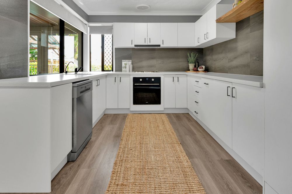 Modern white kitchen with wood accents featuring sleek cabinetry, stainless appliances and natural jute runner on hardwood floors.