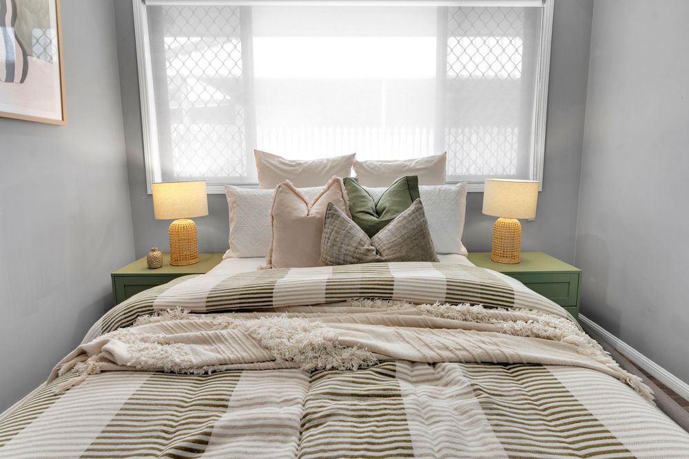 Contemporary bedroom with layered bedding in neutral tones, green pillows, and table lamps on both sides.