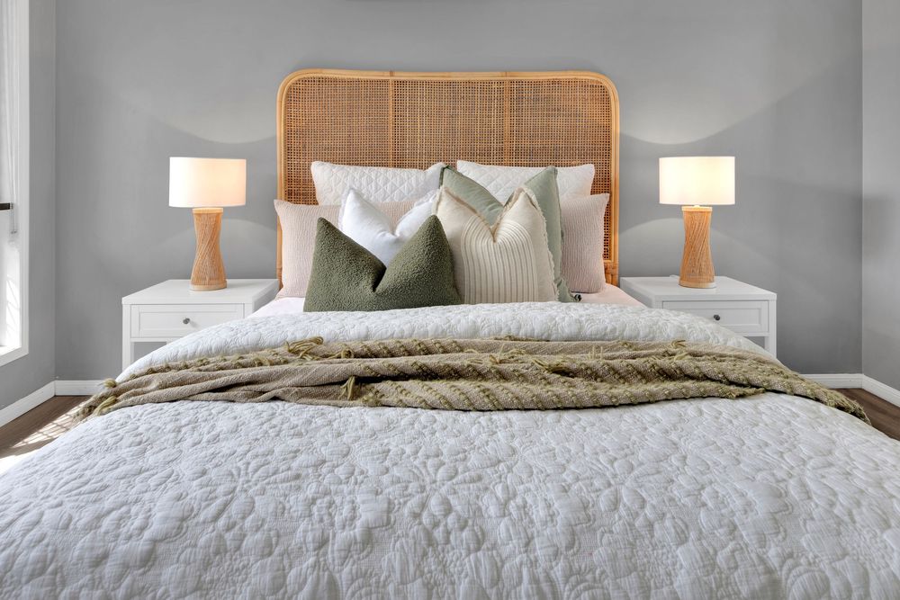 Modern bedroom with white bedding, wooden headboard, and gray walls featuring matching table lamps and throw pillows.