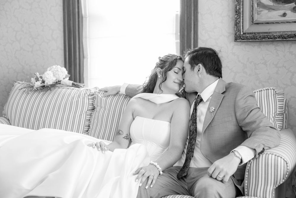 Black and white photo of a bride and groom sharing a tender kiss while seated on an elegant striped sofa.