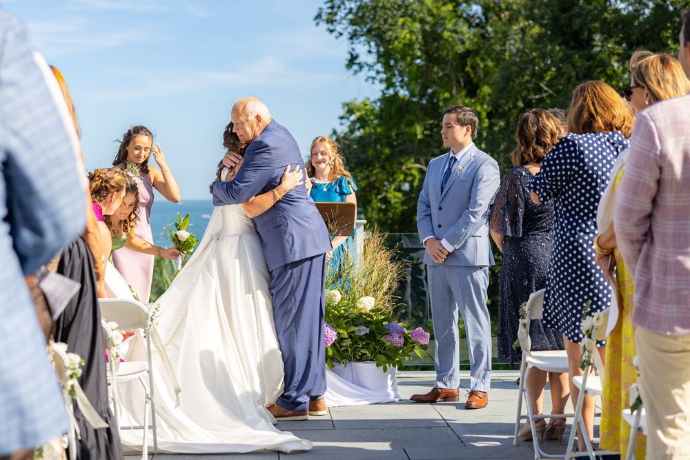Bride and groom share a kiss during outdoor wedding ceremony with guests and officiant on sunny day.