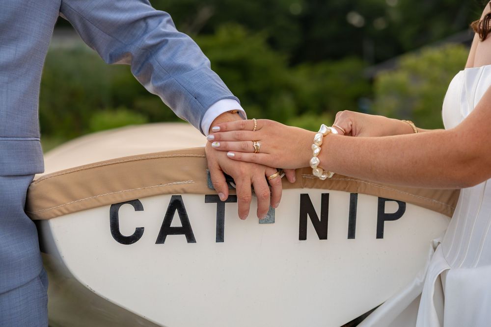 Newlyweds holding hands with wedding rings on a white boat named Cat Nip, bride wearing pearl bracelet.