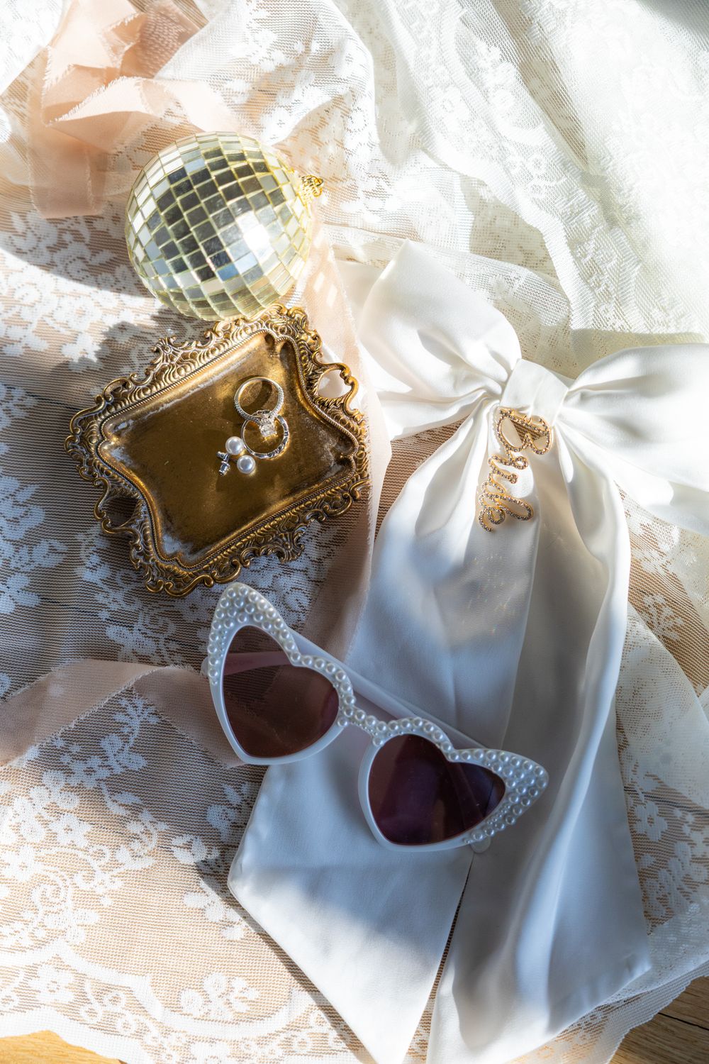Vintage-style wedding accessories including heart-shaped sunglasses, disco ball, and lace details on white fabric.
