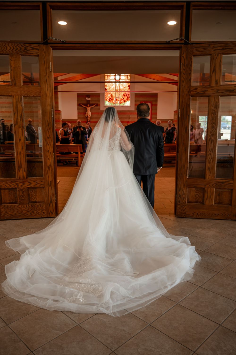 Bride in a long cathedral veil and white gown entering a church with an escort before the ceremony.