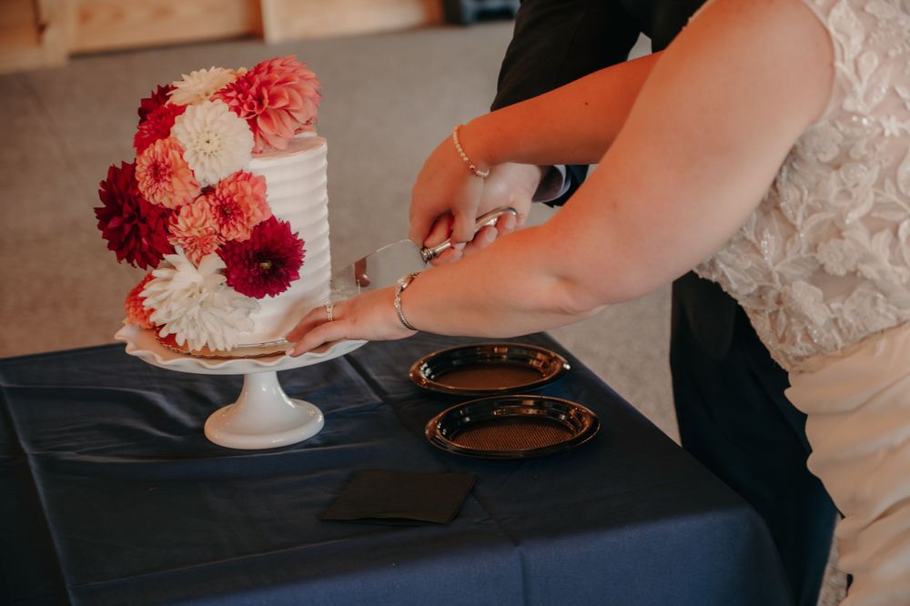 Bride and groom cut their floral wedding cake decorated with red and pink dahlias.