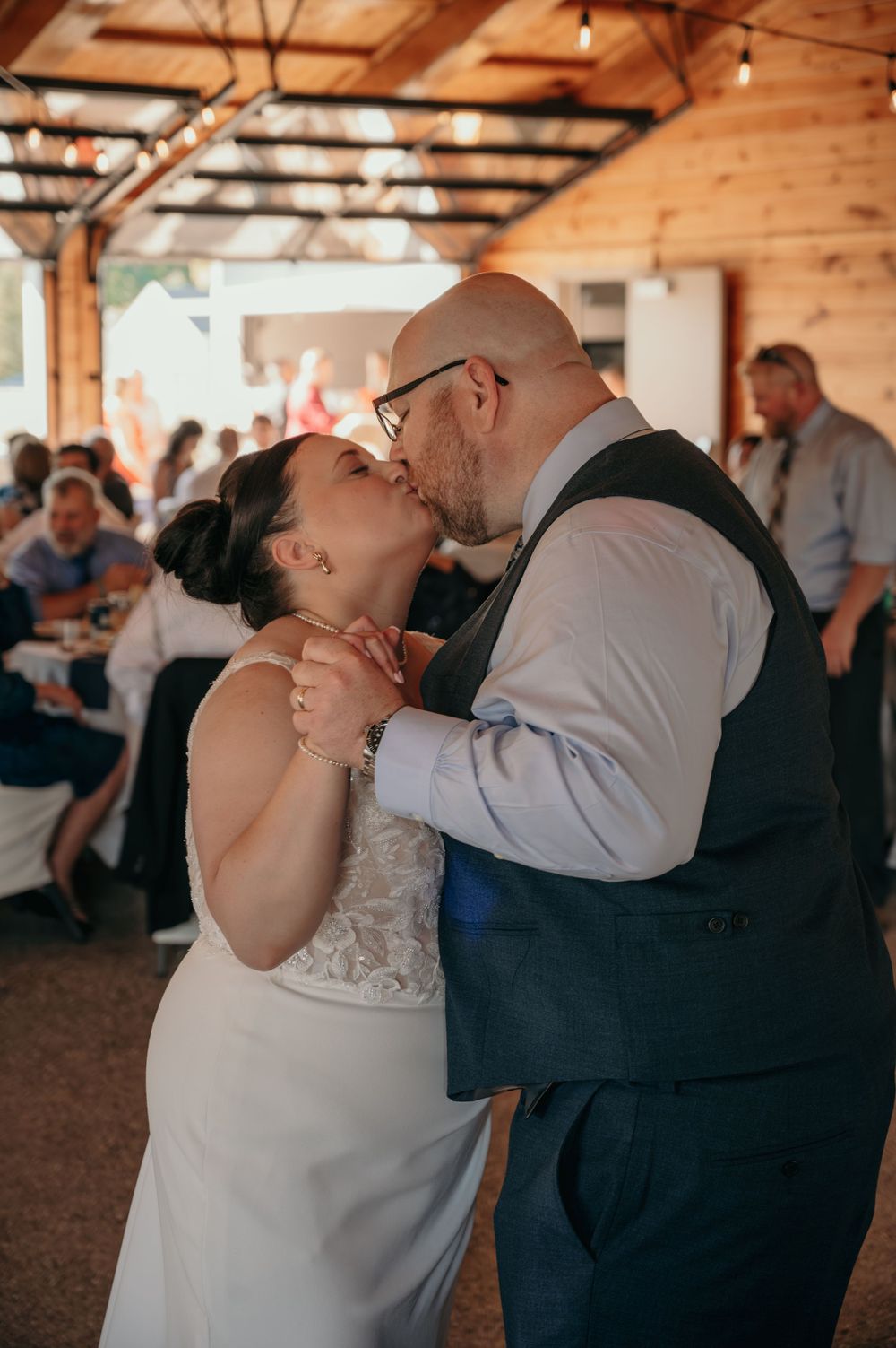 Bride and groom share a romantic kiss during their first dance at rustic barn reception.