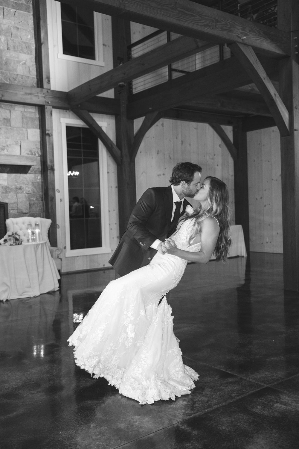 Groom dips bride for a kiss on dance floor inside rustic wooden barn wedding reception venue.