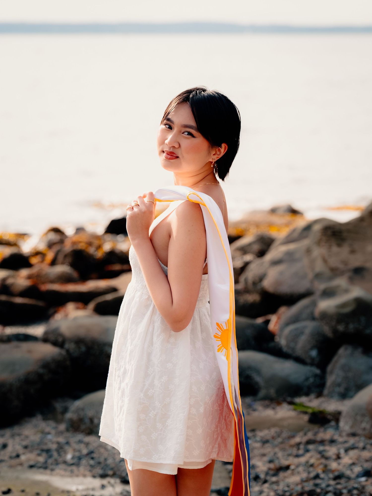 A person in a white dress stands on rocky terrain at sunset.