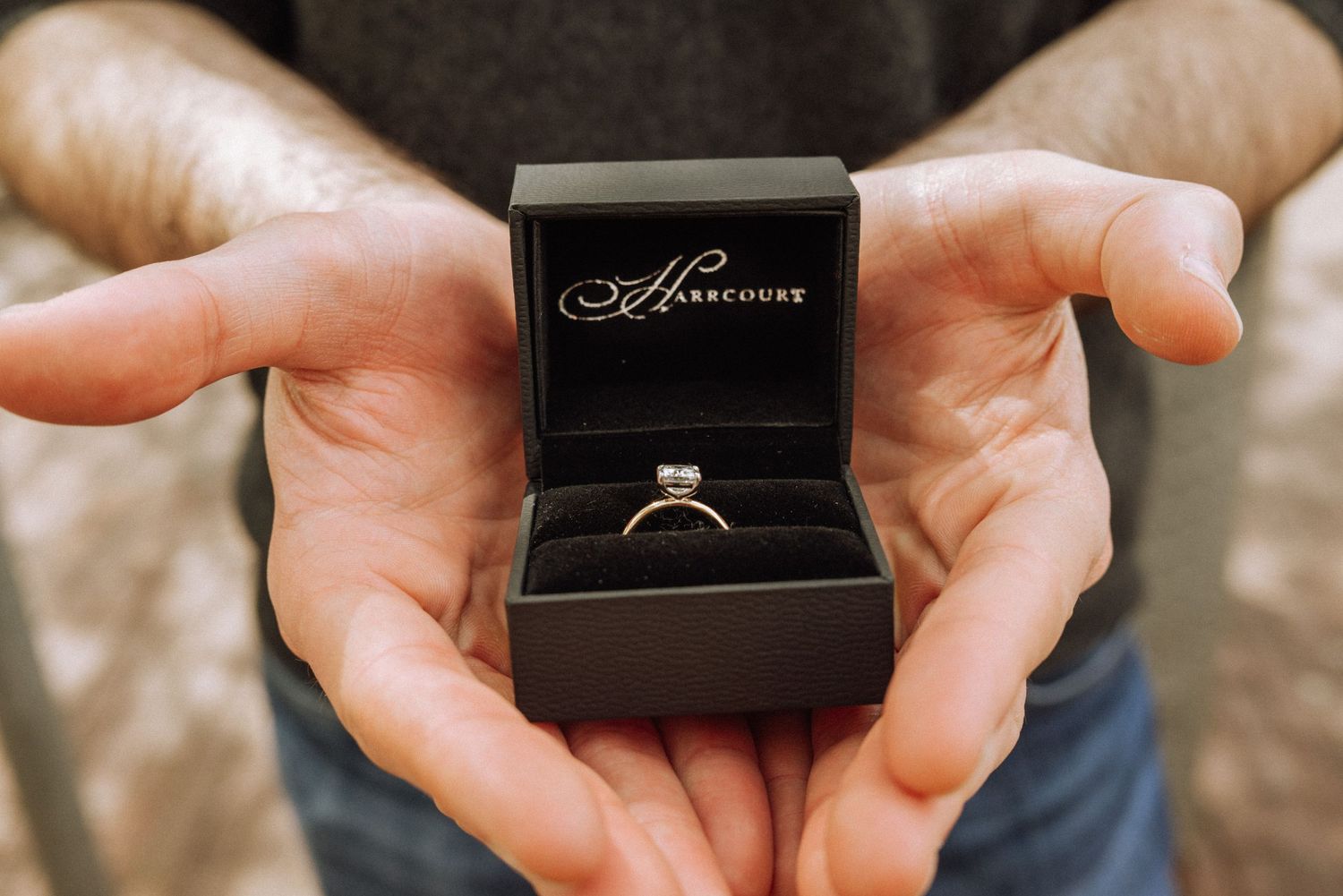Close-up of hands presenting an engagement ring in a black jewelry box.