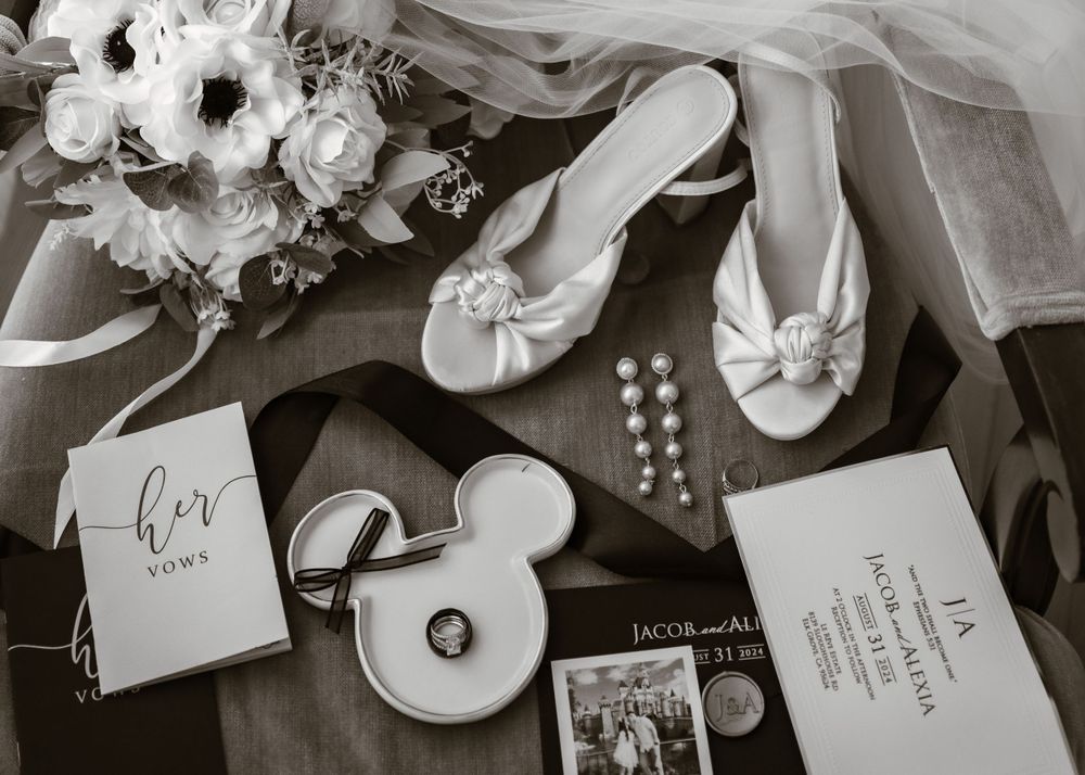Black and white flatlay of wedding stationery, rings, and floral arrangements.