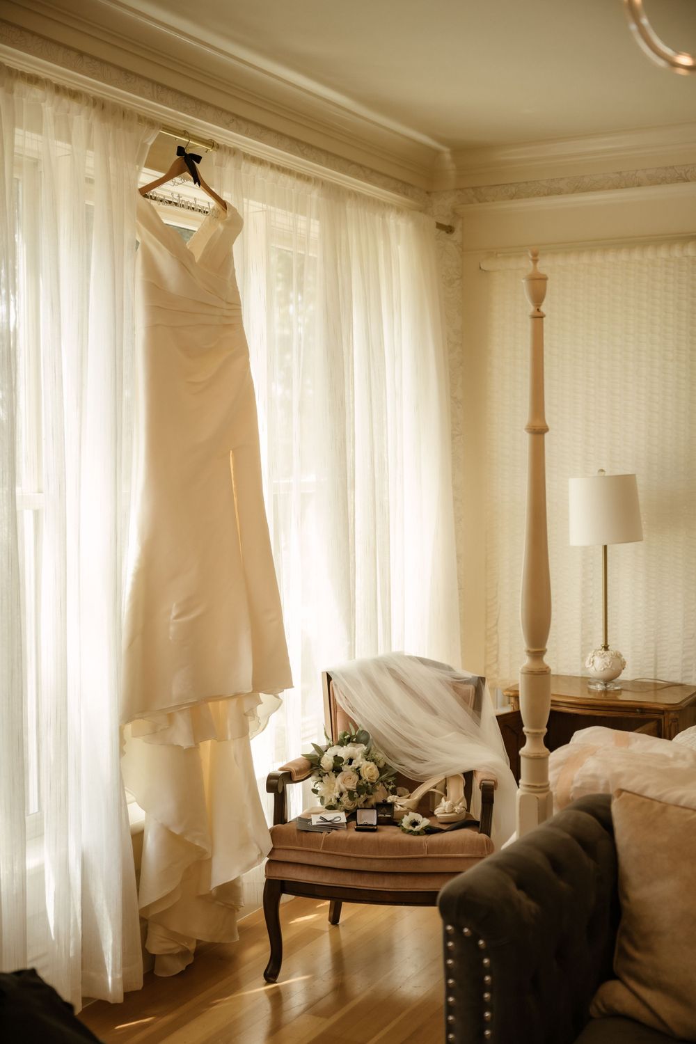 White wedding dress hanging in a bright sunlit room with sheer curtains and elegant decor.