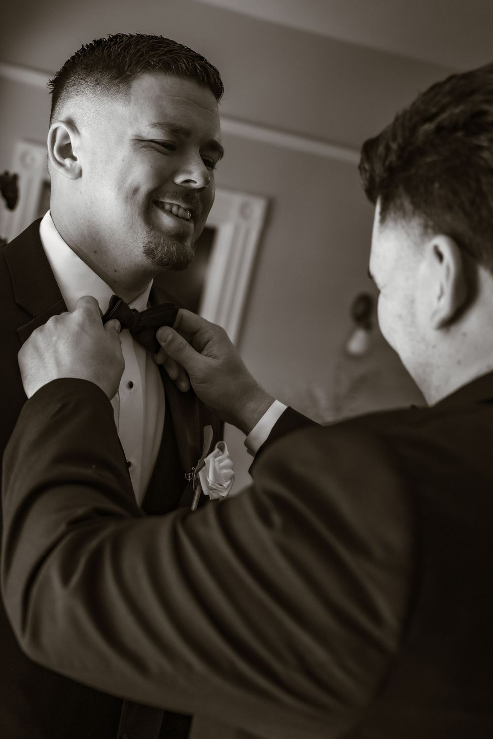 Black and white candid moment of groomsmen adjusting formal attire before ceremony.