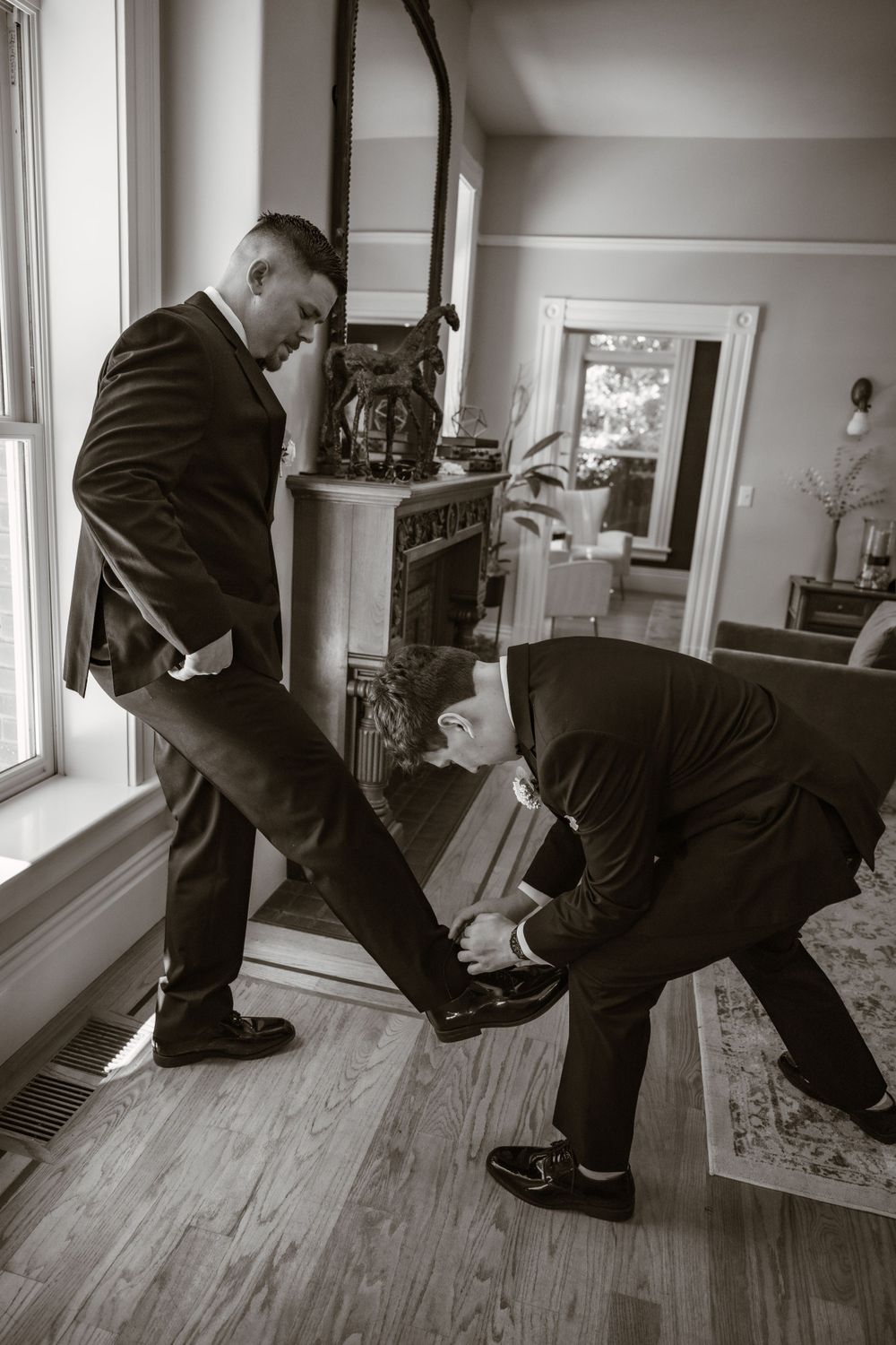 Groomsmen helping each other with formal shoes in preparation for wedding ceremony.