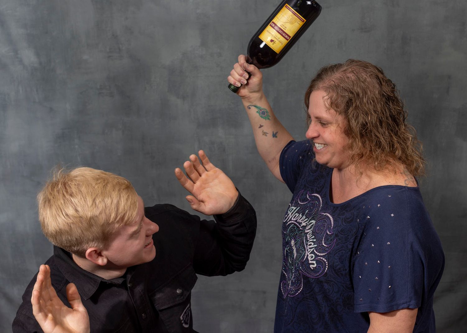Two people acting alarmed in a playful scene with a bottle against a dark gray backdrop.