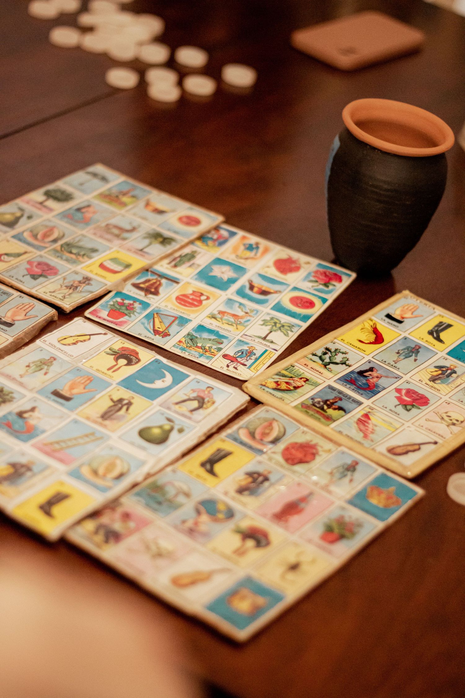 A traditional Mexican Loteria game board laid out on a dark wooden table with a clay cup nearby.