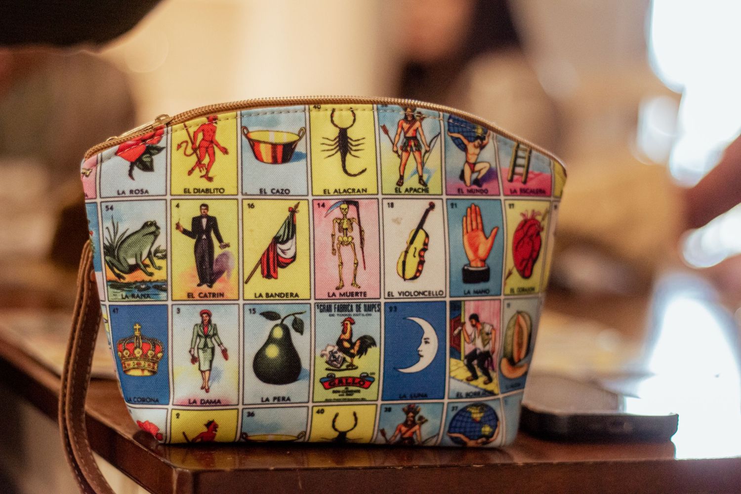 Vintage cosmetic bag featuring colorful Mexican loteria card designs in a grid pattern on light background.