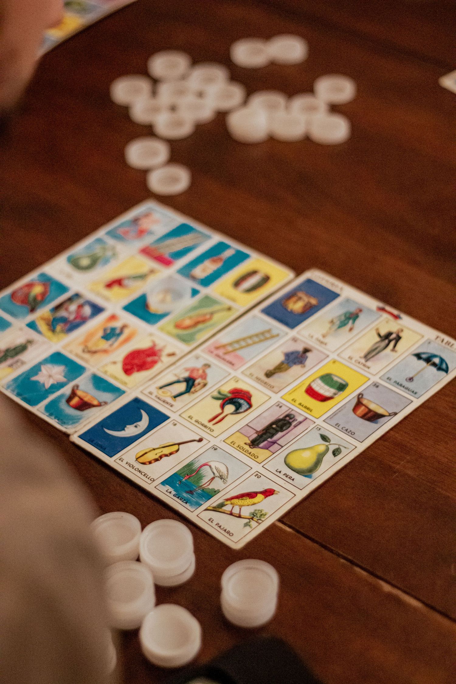 Mexican lottery game cards with colorful illustrated squares laid out on a wooden table with white game tokens.