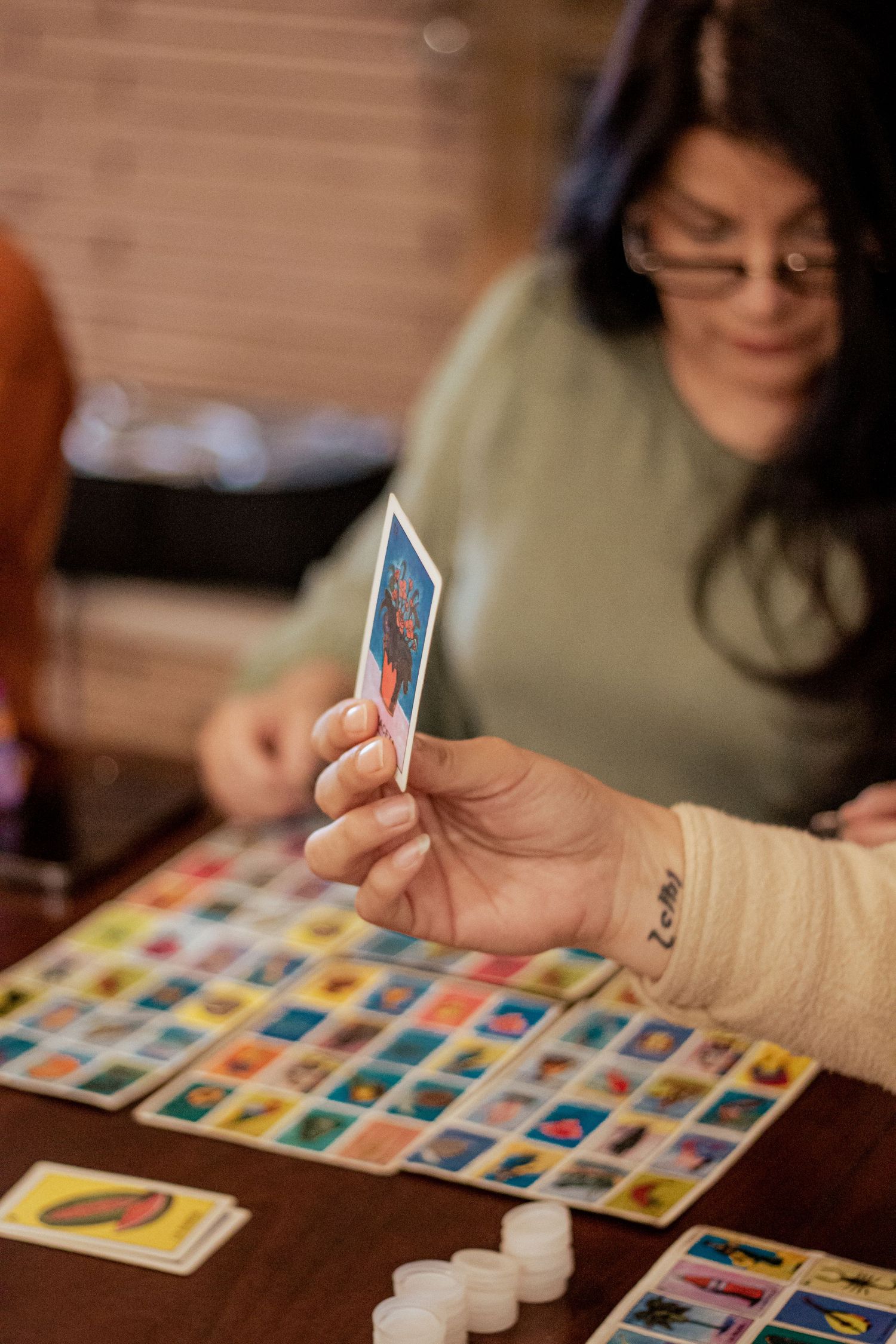 Players engaged in a tabletop game with colorful cards and white tokens on a wooden surface.