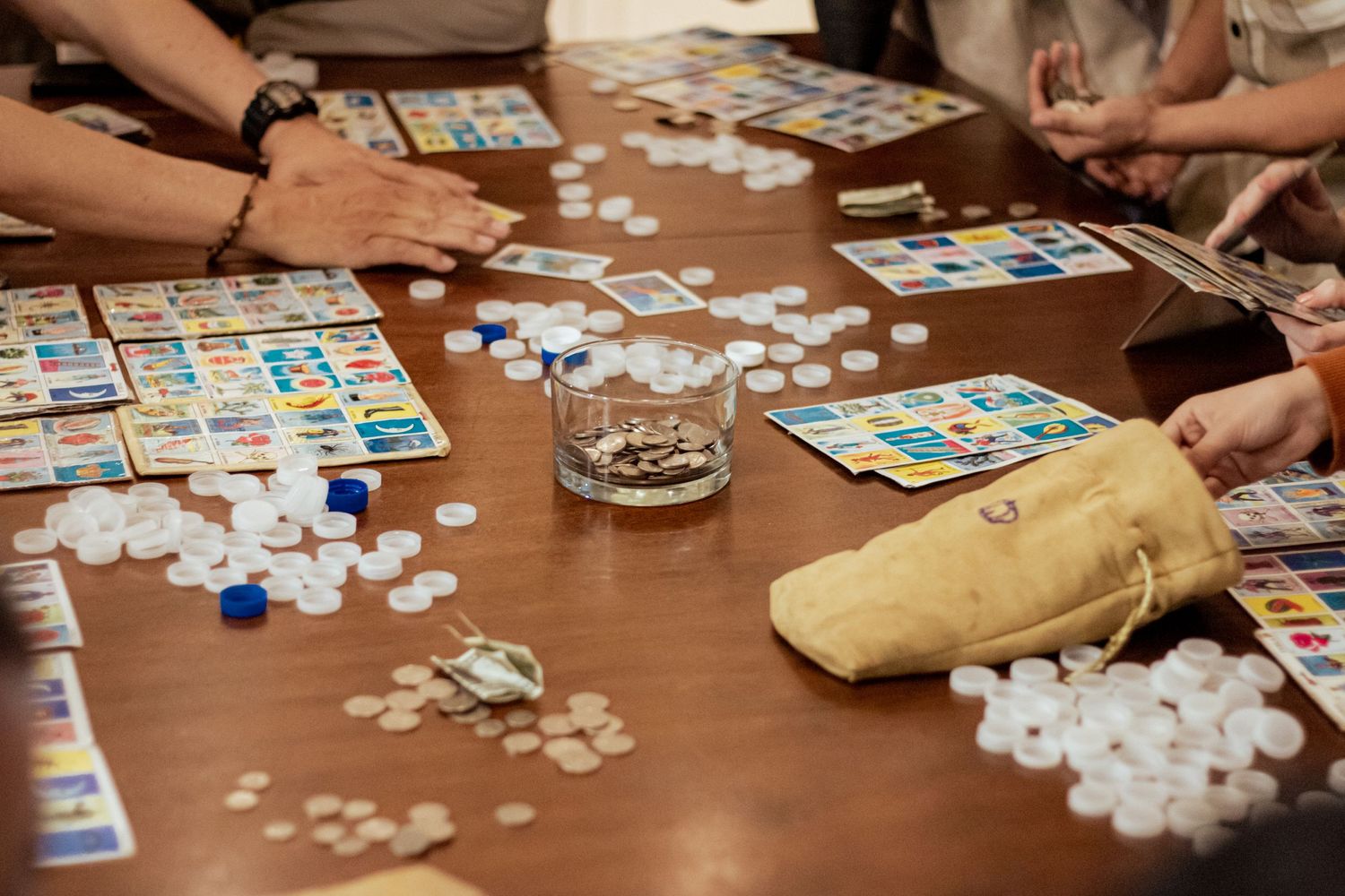 People playing bingo at a wooden table with cards and white chips scattered across the surface.