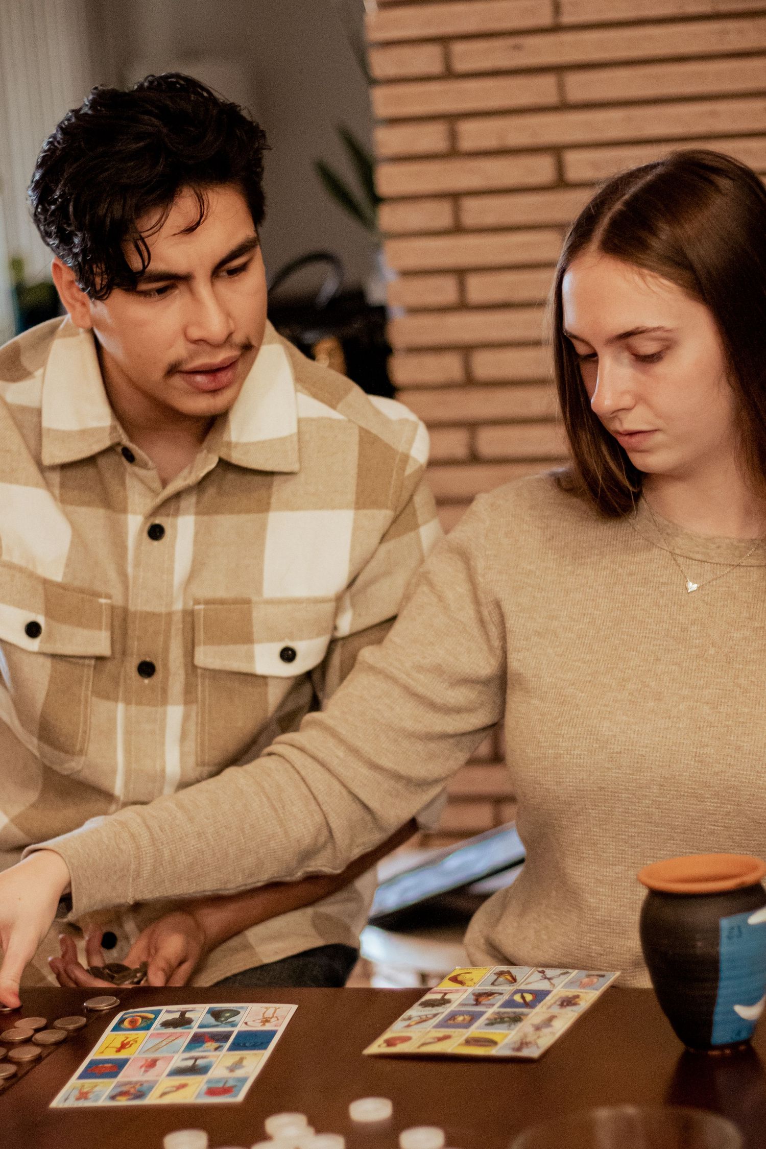 Two people focused on playing a board game at a table with brick wall background.