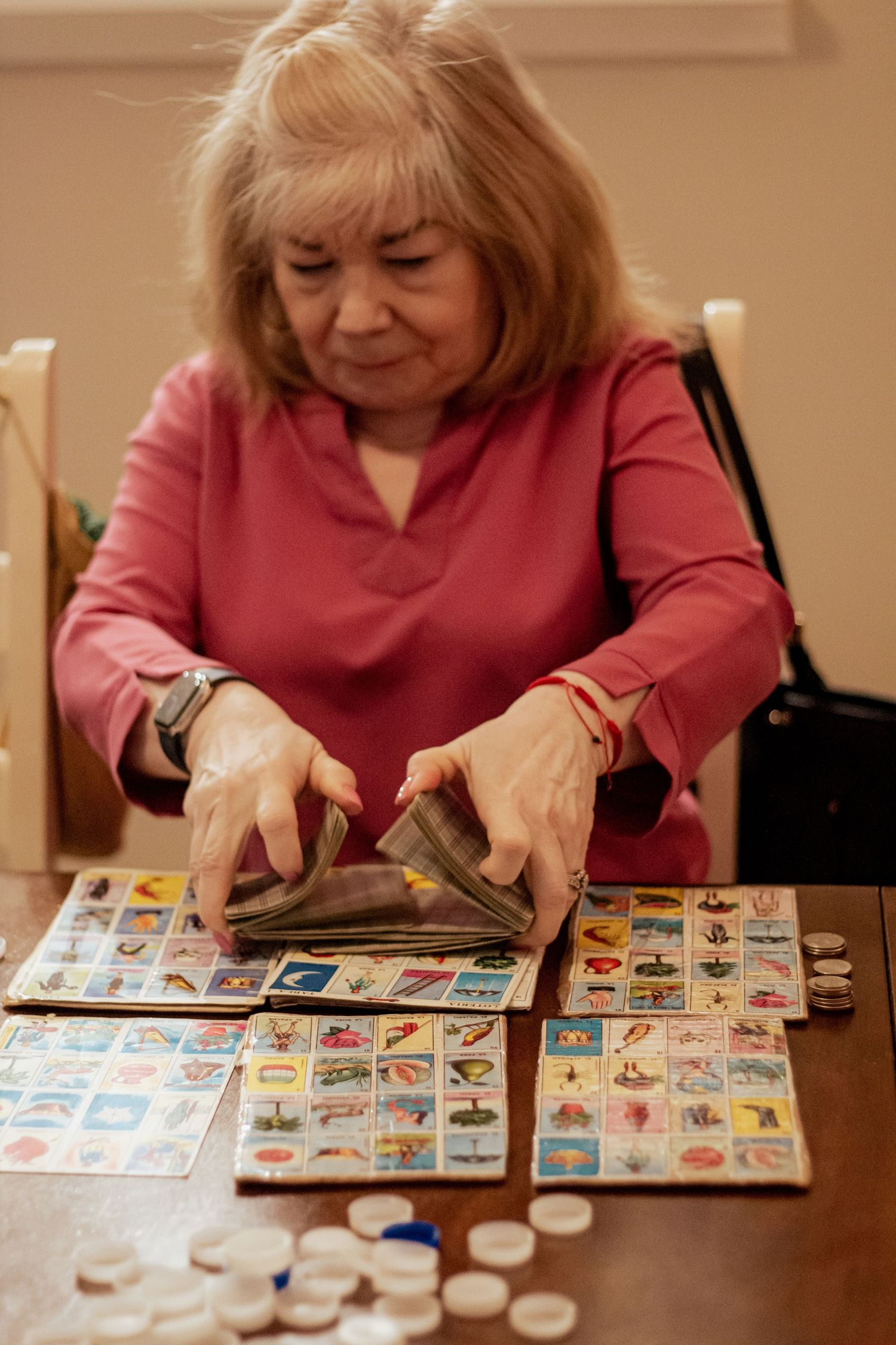Someone wearing a pink sweater plays a game with cards and tokens laid out on a wooden table.