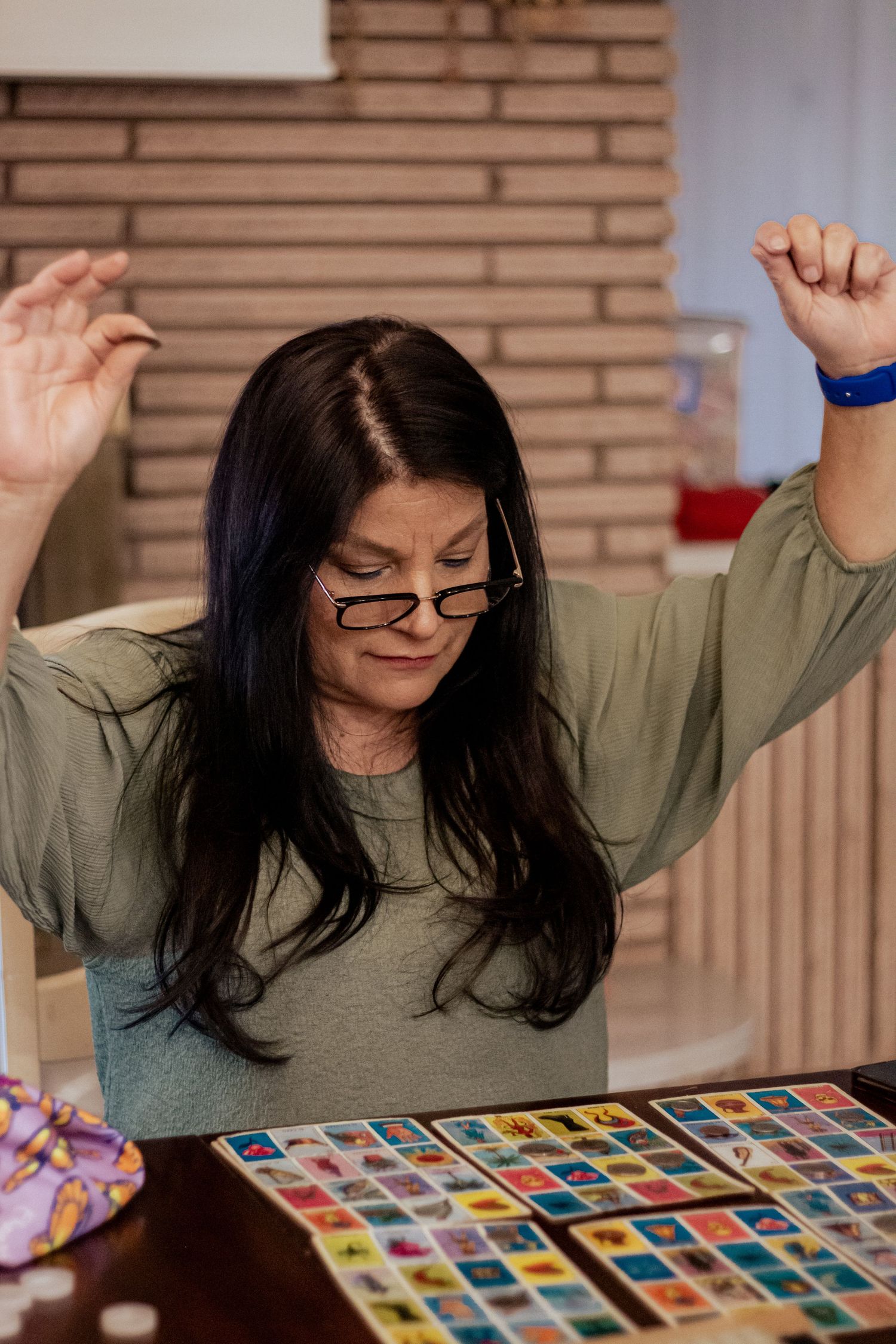 Woman celebrating excitedly while playing a colorful card game at a table.