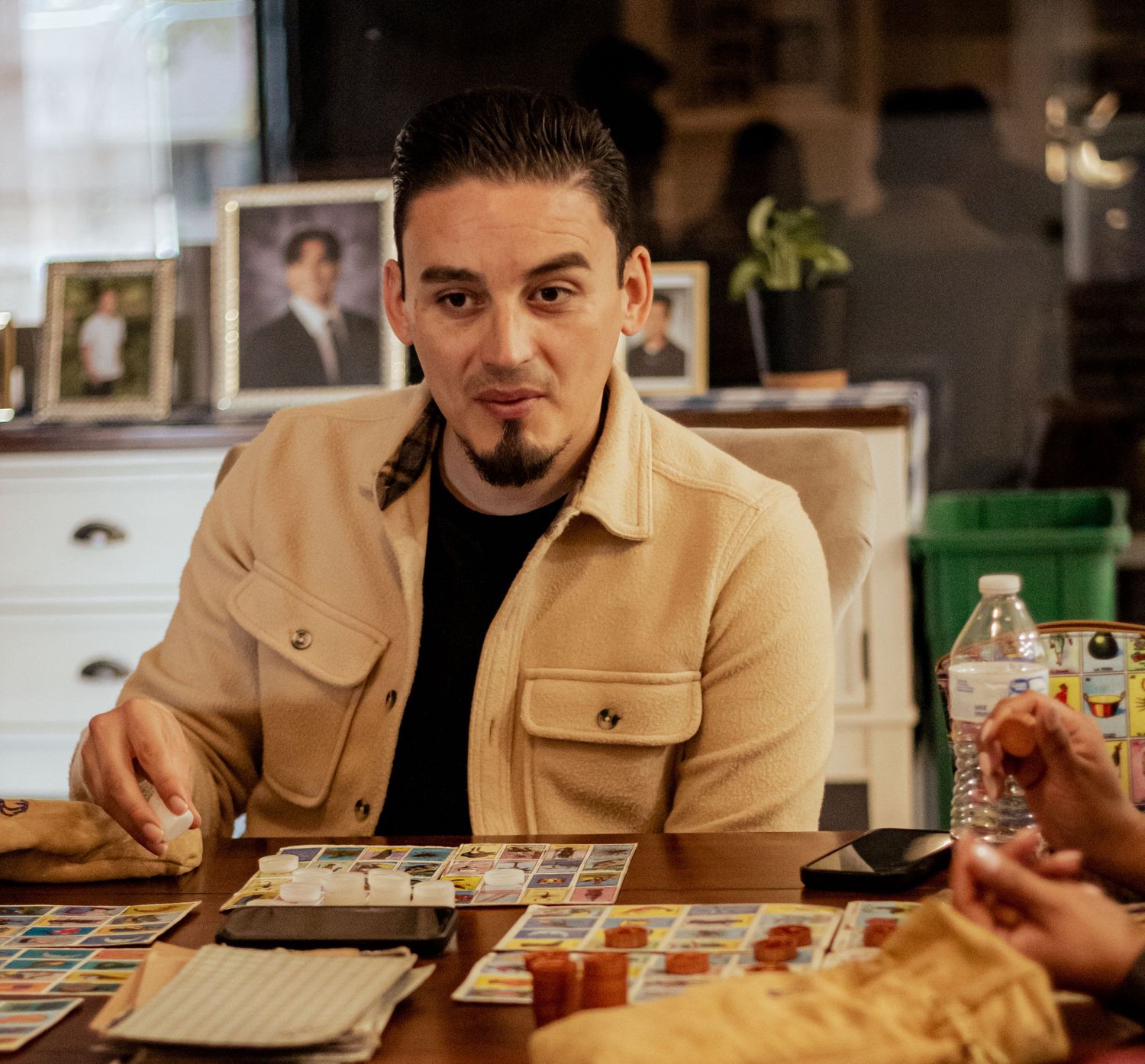 Someone sitting at a table wearing a tan jacket and black shirt while playing a board game with friends.