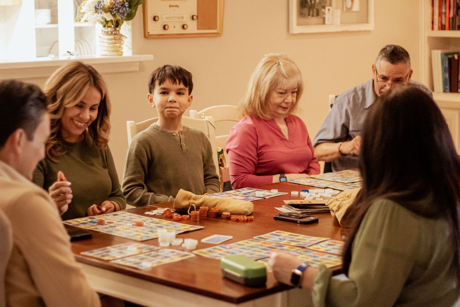 Family gathered around a table playing board games or cards together in a cozy living room.