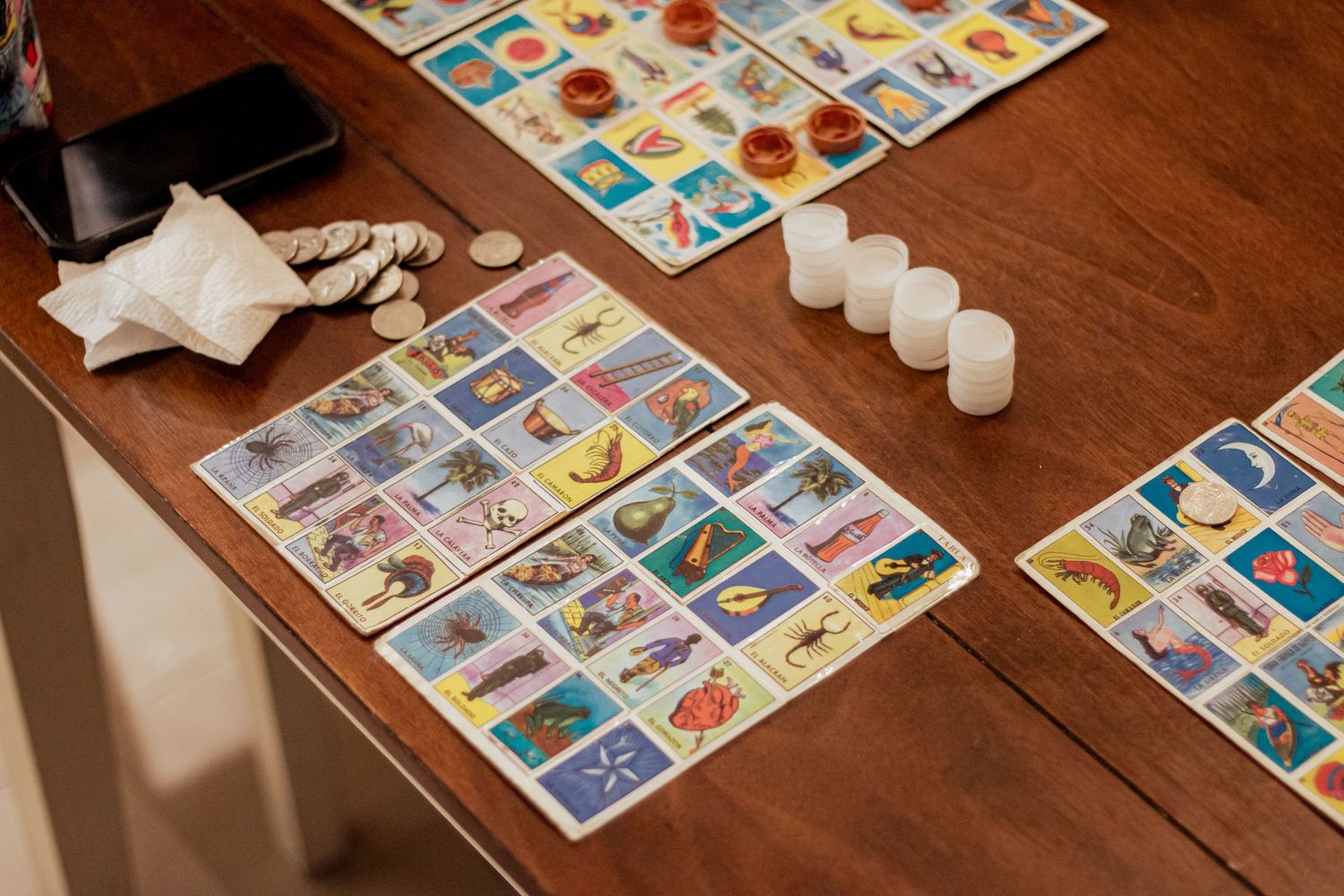 Colorful loteria game cards and playing pieces laid out on dark wooden table surface.