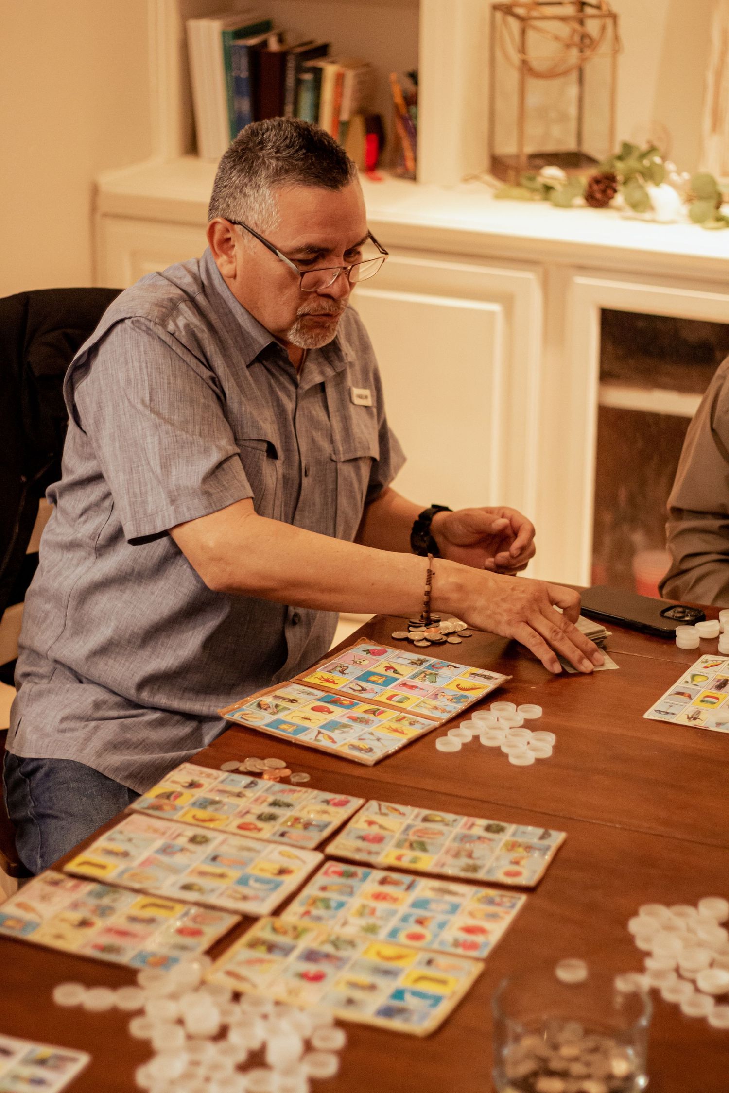 Players focused on multiple bingo cards spread across a wooden table during an evening game.