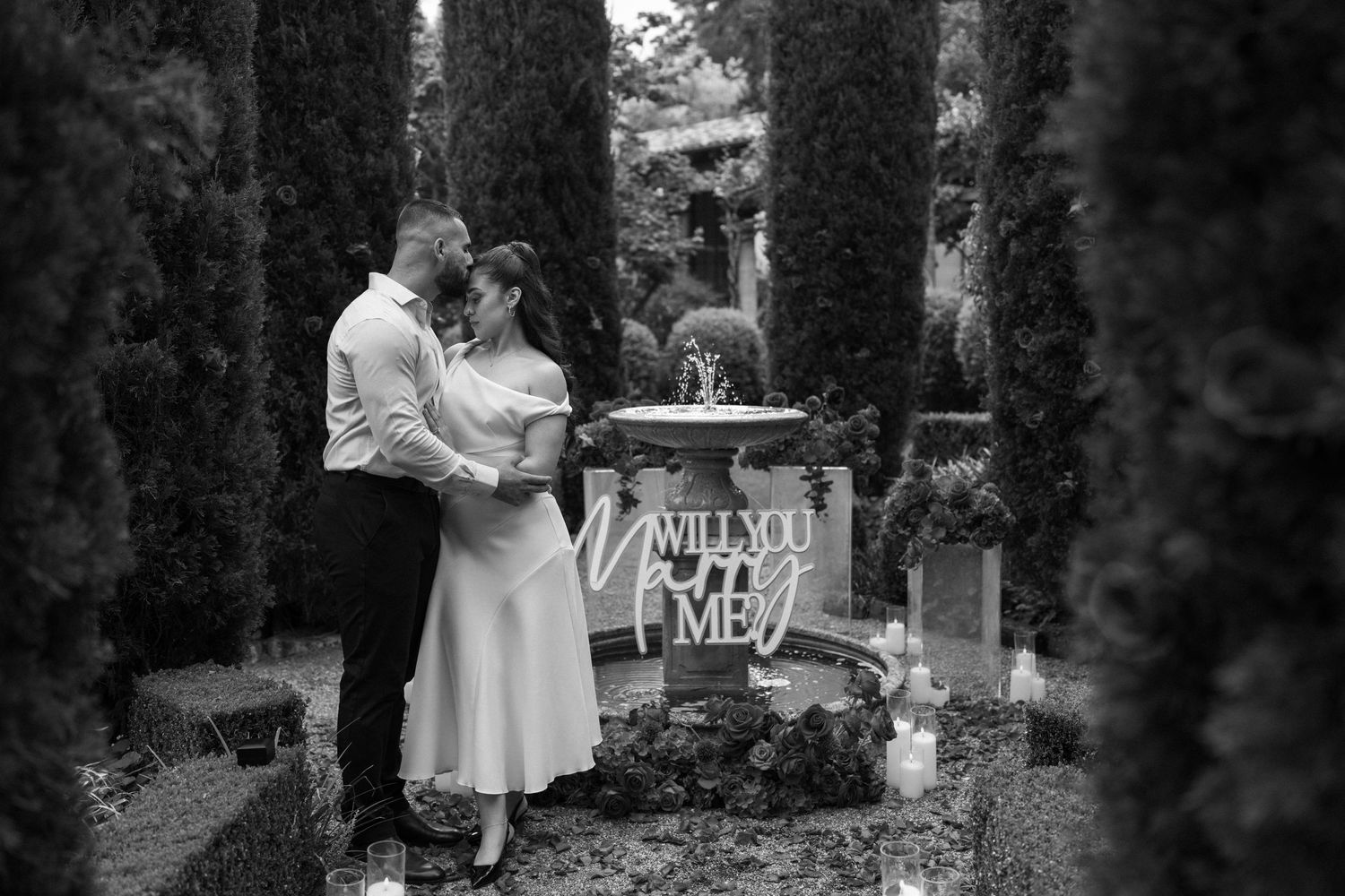 Black and white image of a couple standing by a decorated table in a cypress garden.