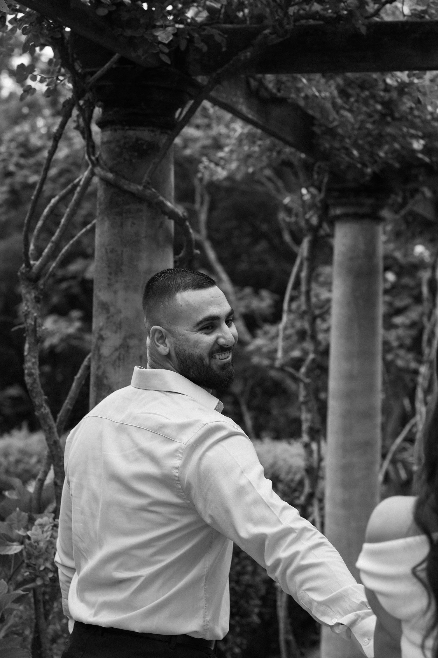 Black and white photo of a person in a white shirt smiling in a garden with columns.