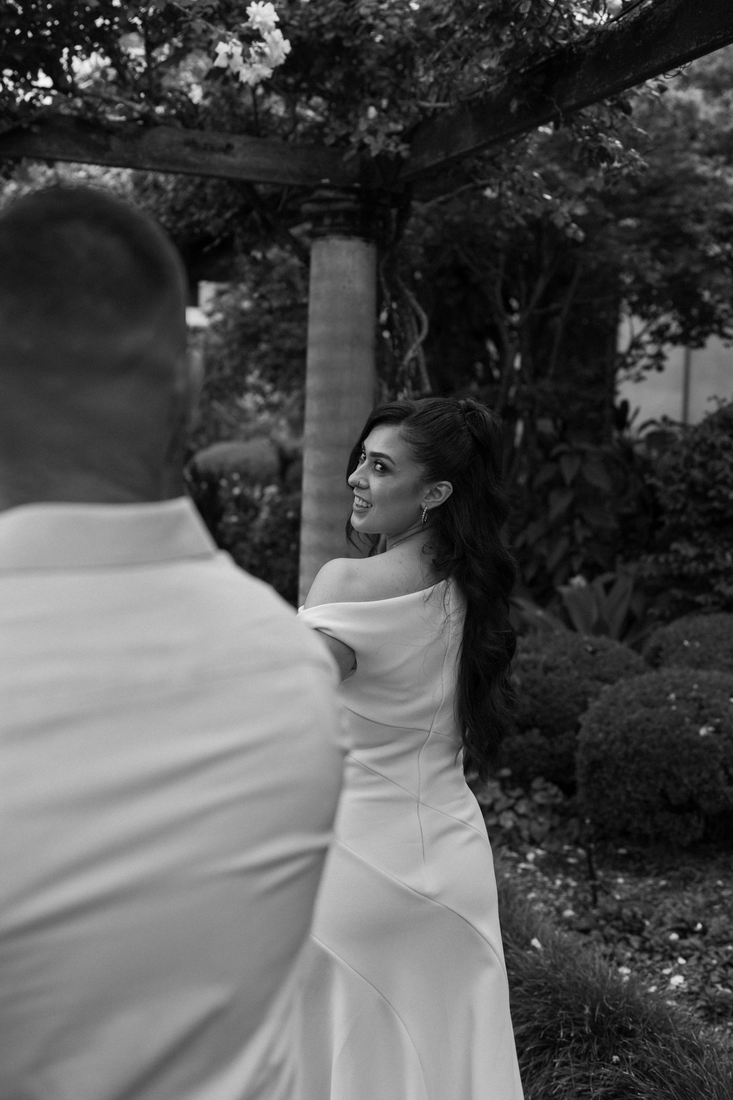 Black and white portrait of two people in an intimate moment surrounded by garden foliage.