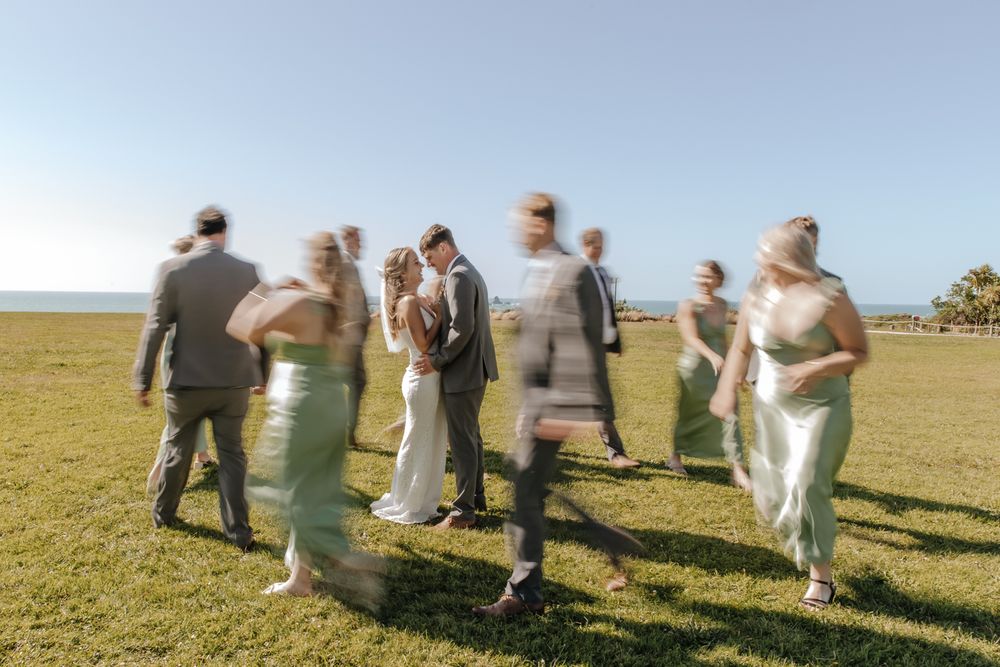 Newlyweds celebrating with bridal party on a rugged West Coast NZ landscape, during a fun and candid moment