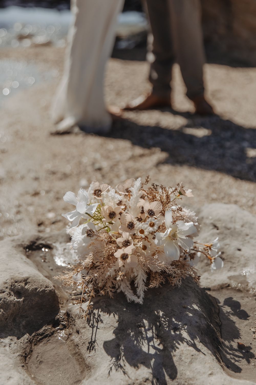 close up of details of brides bouquet during a West coast beach beach wedding while couple have romantic intimate moment