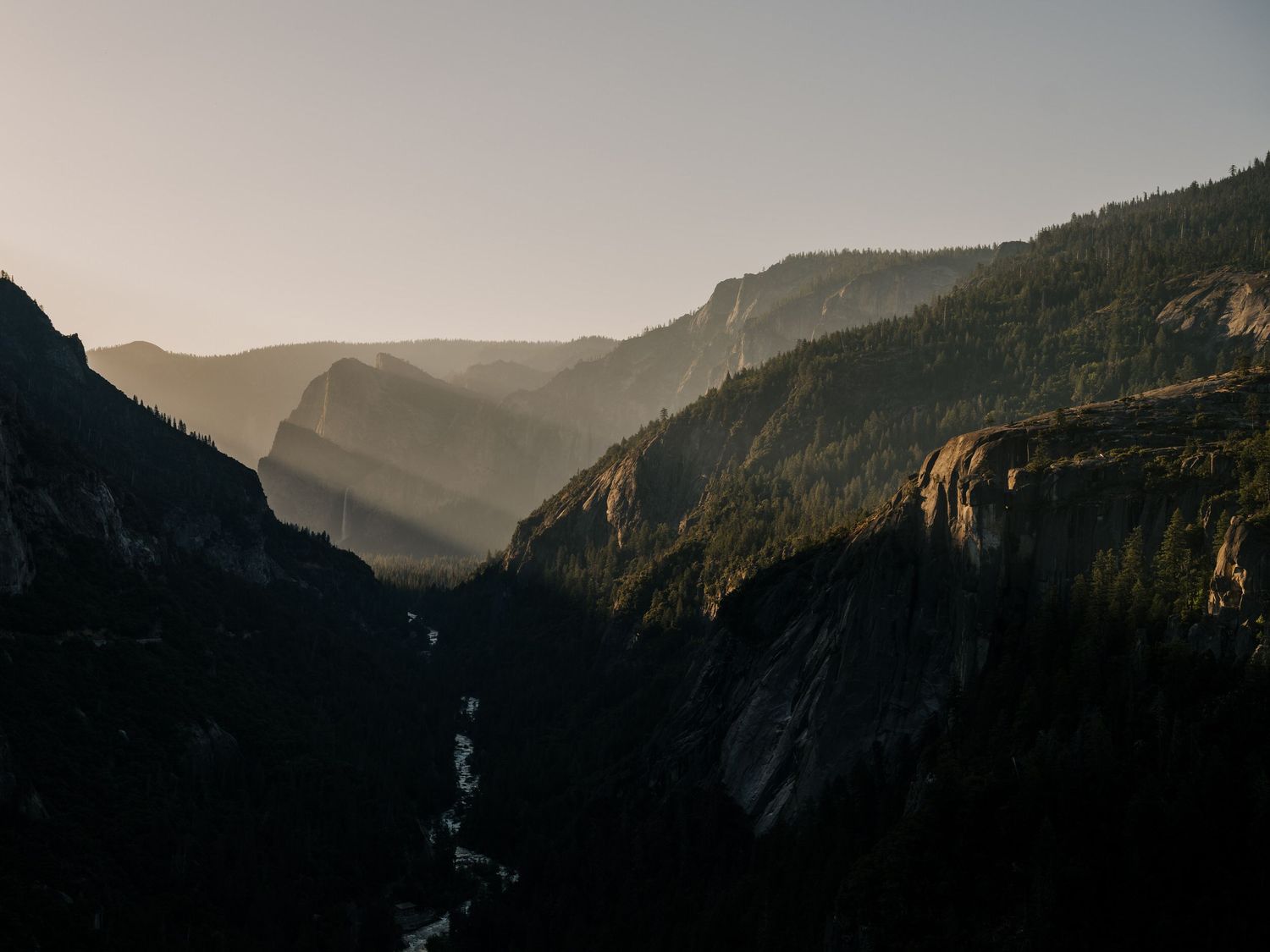 Aerial view of Yosemite Valley's rugged mountain landscape with deep valleys and winding river during golden hour.