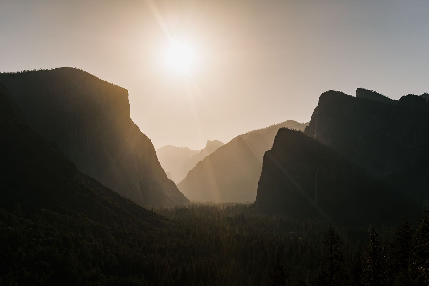 Dramatic silhouette of Yosemite Valley's iconic granite cliffs and peaks at sunset with sun creating ethereal backlighting.