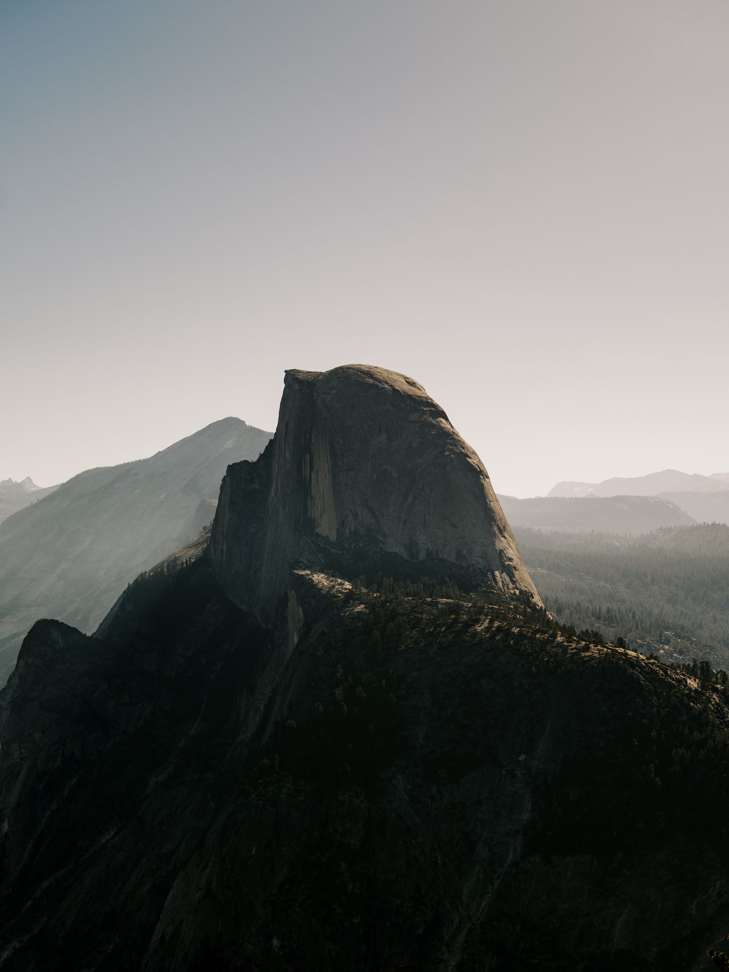Dramatic view of Half Dome mountain peak silhouetted against a hazy sky in Yosemite National Park at sunrise.